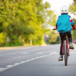 Child,With,Rucksack,Riding,On,Bikes,In,The,Park,Near